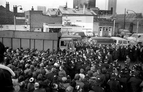 A crowd of striking workers facing off with police on the street [BBC News]