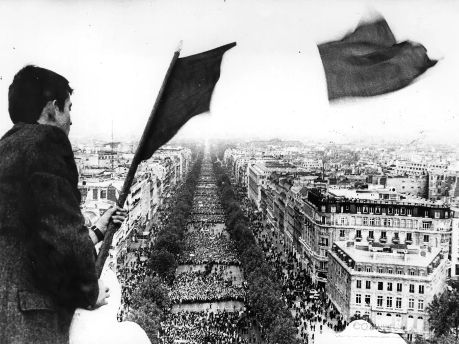 A man flies the French tricolor flag over crowds marching to the Arc de Triomphe during the Paris students' strike. [npr.org]