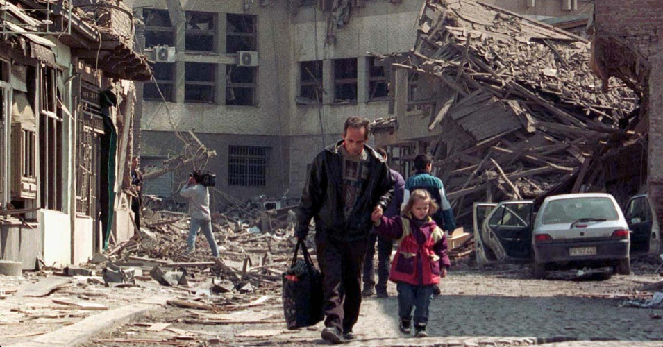 A man leads his daughter away from destroyed buildings after NATO air strikes hammered the center of Pristina, the Kosovo capital. Photo credit to Goran Tomasevic/Reuters. [rferl.org]
