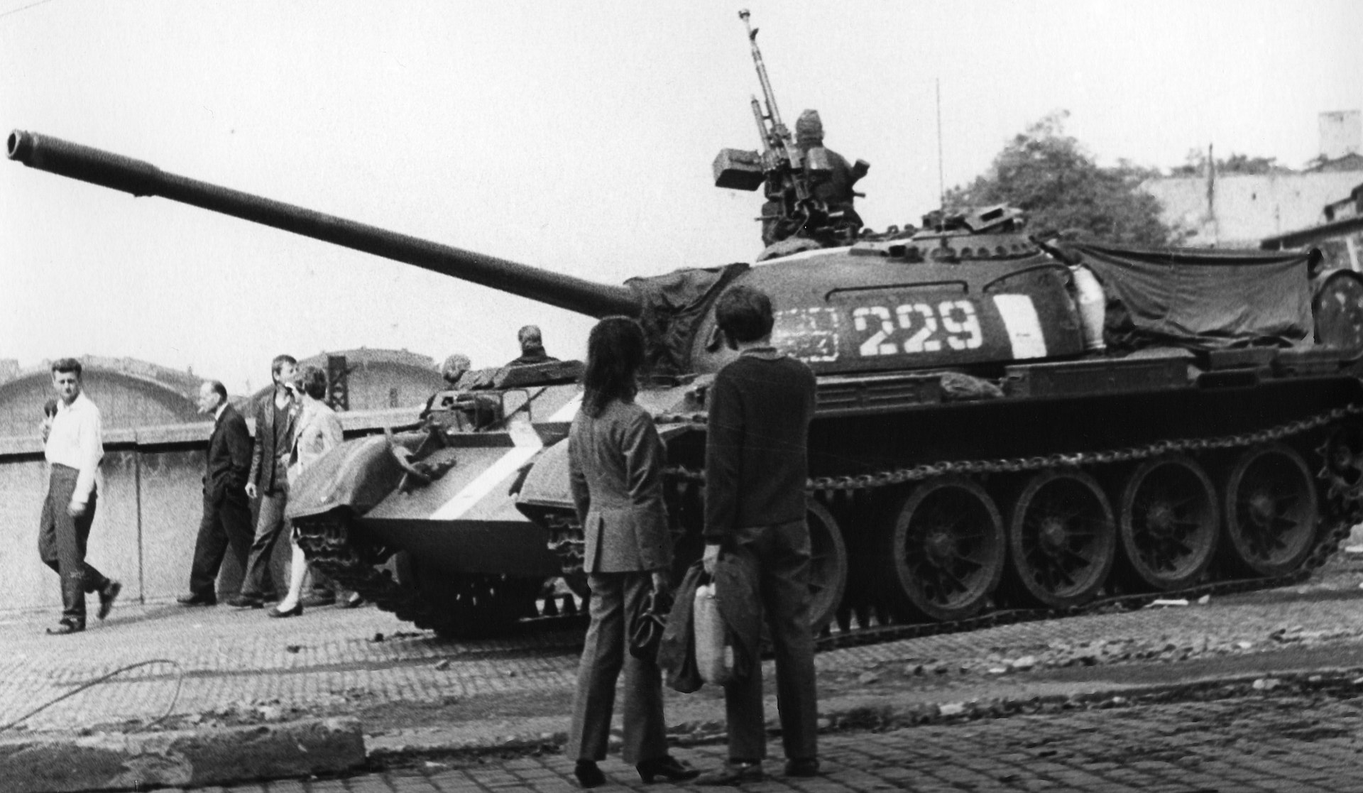 A group of civilians look at a tank on what appears to be a city street
